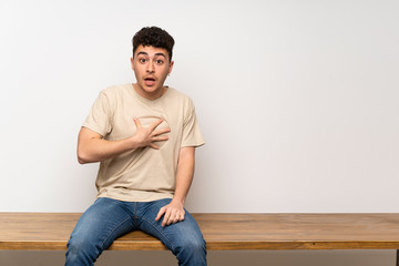 Young man sitting on table surprised and shocked while looking right