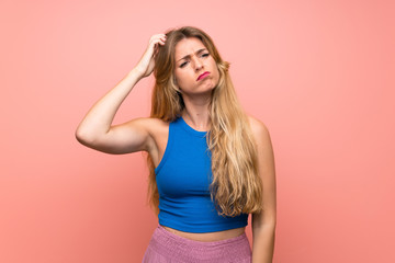 Young blonde woman over isolated pink background having doubts while scratching head