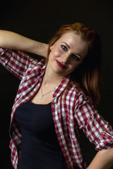 Low key portrait of beautiful young woman looking at the camera posing with hand behind her hand dressed in a black tank top and plaid shirt. 