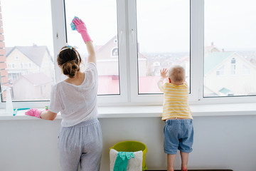 Mother of a toddler boy is cleaning plastic window door with wet cloth