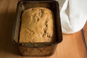 Banana bread in loaf tin on rustic wooden table with dish towel