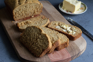 Banana bread loaf with slices and butter  on wooden board on grey