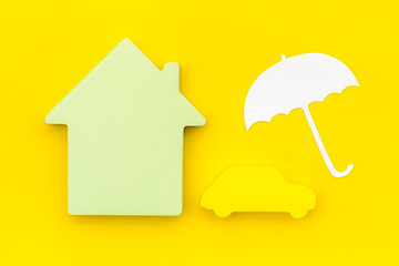 buying new auto concept with car toy, house and umbrella figure on yellow background top view