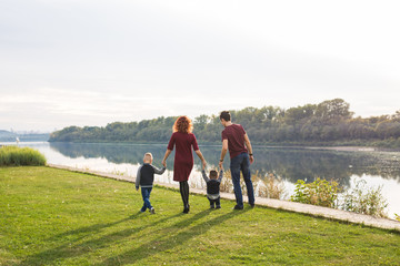 Fototapeta premium Parenthood and nature concept -Family of mother and father with two boys twins kids in a park at summer by a river at sunny day
