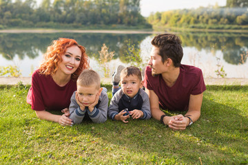 Parenthood, nature, people concept - family with two sons lying near the lake