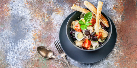 Caesar salad with chicken, cherry tomatoes, croutons and basil in a dark blue bowl on a rusty background. Top view