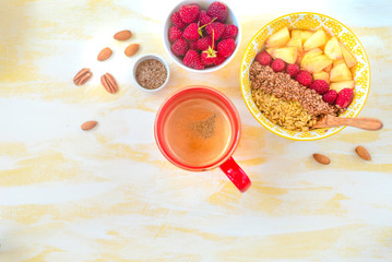 Top view, female hands holding a cup of coffee, a spoon with oatmeal, with honey nuts, raspberries, on a yellow wooden table Good morning - healthy breakfast background
