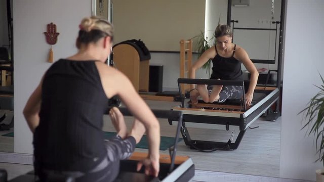 An athletic woman is practicing stretching exercises on the reformer gym
