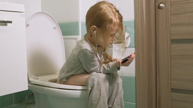 little girl sits on the toilet and uses the phone