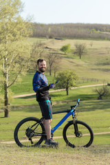 Obraz premium Cyclist in shorts and jersey on a modern carbon hardtail bike with an air suspension fork rides off-road on green hills near the forest