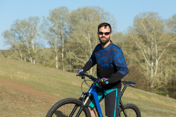 Obraz premium Cyclist in shorts and jersey on a modern carbon hardtail bike with an air suspension fork rides off-road on green hills near the forest