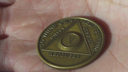 Hand opening and showing Alcoholics Anonymous medal with 5 years of sobriety