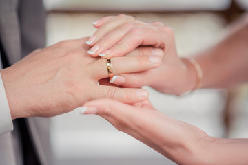 At the wedding, the bride and groom help each other by putting the wedding rings on the ring finger. Close-up.