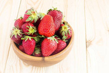 Strawberries in a bowl on a light wood background with place for text. Berry summer background.