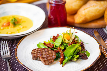  beautiful grilled steak, with green salad, sun-dried tomatoes and physalis on a white plate.  dinner.  dinner table.