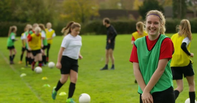 4K Portrait smiling girl, youth soccer player with teammates training in background