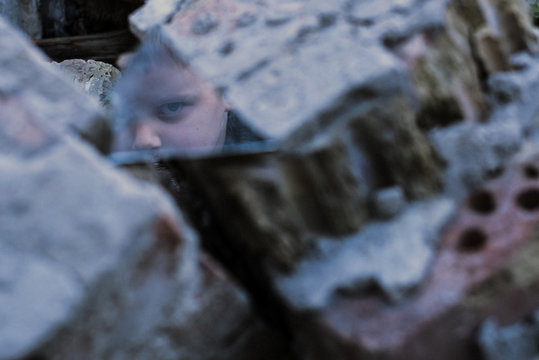 reflection of an evil child's face in a fragment of a mirror in the ruins