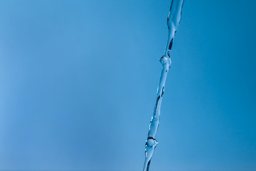 Transparent jet of water against a blue background. Cold water, ice water. The glare of light is reflected in the flow of water.