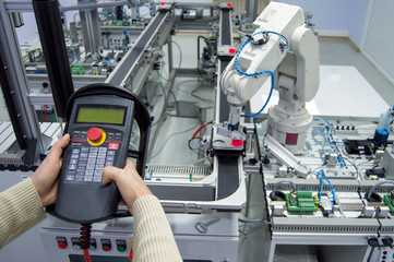 Man is pushing button on teach panel  to control a robotic arm which is integrated on smart factory production line. industry 4.0 automation line which is equipped with sensors and robotic arm.