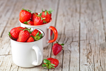 Organic red strawberries in two white ceramic cups on rustic wooden background. Healthy sweet food, vitamins and fruity concept.