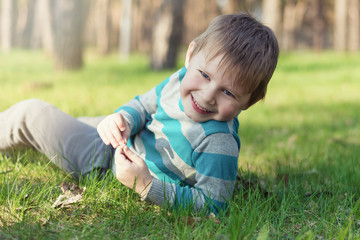 A little boy is smiling and lying on the green grass in the park.