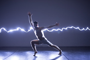 Modern Dance performer dancing with a neon blue light while making gracious moves and spectacular body art expressions, long exposure motion blur