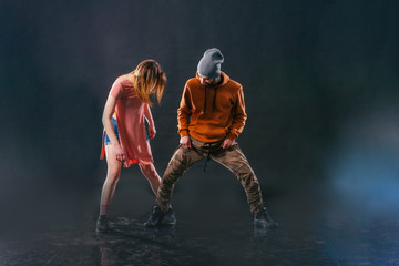 Couple dancing modern dance and showing off their leg stretch moves.Black background while the couple is dressed in urban colorful clothes...