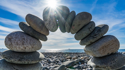 Stone arch on the shore of the Black Sea. Sun disk and blue sky on background, Sochi, Russia.