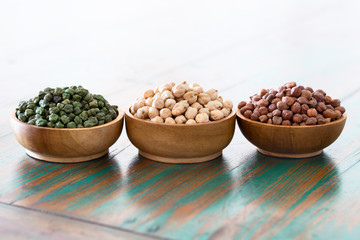 Colored chickpeas (red, green, white) in wooden bowls on rustic background.