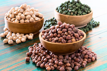 Colored chickpeas (red, green, white) in wooden bowls on rustic background.