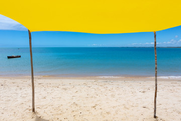 Obraz na płótnie Canvas Beautiful beach view from inside yellow tent on sunny summer day. Sea and blue sky in the background. Concept of vacations, peace and relaxation. Ponta do Corumbau beach, Bahia, Brazil.