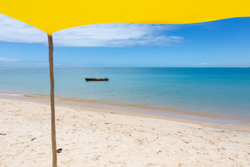 Beautiful beach view from inside yellow tent on sunny summer day. Sea and blue sky in the background. Concept of vacations, peace and relaxation. Ponta do Corumbau beach, Bahia, Brazil.