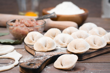 Raw dumplings on the cutting board and ingredients for their preparation on a wooden table