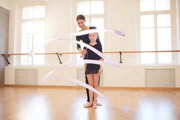Obraz premium Full length portrait of teacher helping little girl doing ballet moves in studio lit by sunlight, copy space