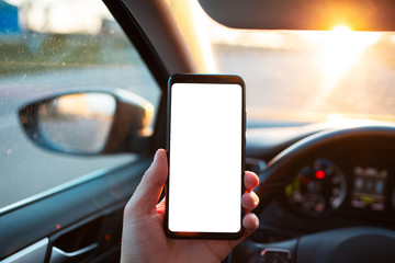 Man holds a smartphone with mockup in the car on sunset background