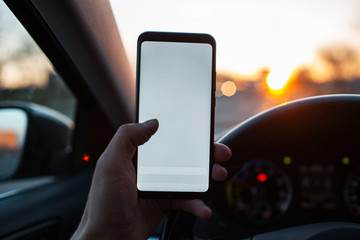Man holds a smartphone with mockup in the car on sunset background