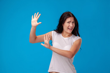 Studio portrait of a young beautiful woman in a white t-shirt against a blue wall background. People sincere emotions.