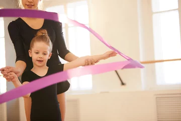 Wandaufkleber Little girl doing gymnastics moves with ribbon in studio lit by warm sunlight, copy space © Seventyfour