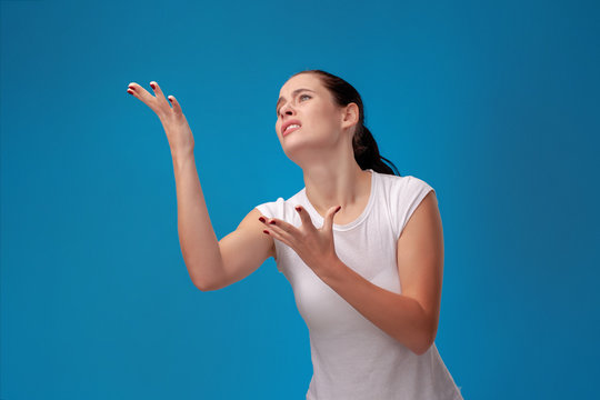 Studio portrait of a young beautiful woman in a white t-shirt against a blue wall background. People sincere emotions.