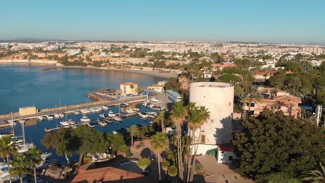 Drone flight over the tower of Cabo Roig and the boat harbor in the warm morning light on the Costa Blanca south of Torrevieja.