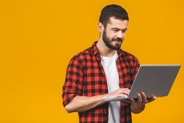 Concentrated on work. Confident young handsome man in casual working on laptop while standing...