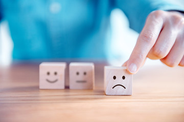 Close up customer hand choose sad face and blurred smiley face icon on wood cube, Service rating,...