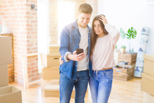 Beautiful Young Couple Moving To A New House Using Smartphone Stressed With Hand On Head, Shocked With Shame And Surprise Face, Angry And Frustrated. Fear And Upset For Mistake.