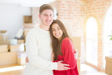 Beautiful young couple moving to a new home, standing on new aparment around cardboard boxes, hugging smiling happy and in love