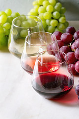 Variety of wine. Red, rose and white wine in old fashion glasses with bunches of grapes on white marble table