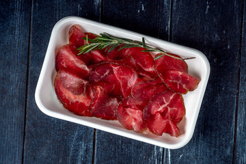 Cut into pieces smoked bresaola on a plastic plate. Italian antipasti prosciutto