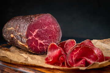 Half a smoked bresaola and cut pieces on a chopping Board. Italian Antipasti, rustic style