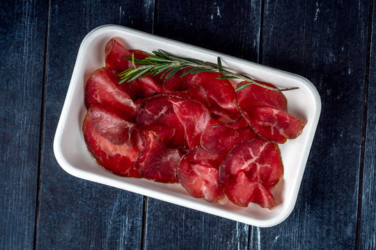 Cut into pieces smoked bresaola on a plastic plate. Italian antipasti prosciutto
