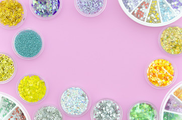 Sequins and glitters for nails in jars with border arrangement. Top view on a pink background with copy space