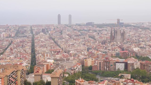 Nice view of Barcelona from height, dense build urban area, straight streets crossing residential quarters. Mediterranean sea seen foggy at horizon. Sagrada Familia under construction